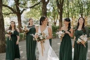 Bride and her bridesmaids on their way to the ceremony laughing and carrying their bouquets The bridesmaids are in emerald green