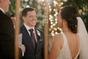 Groom and bride smiling at each other at the altar as the officiant looks on at the garden setting