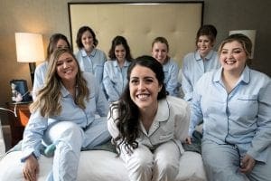 Bride and her bridesmaids smiling at the camera in their pajamas sitting on a bed