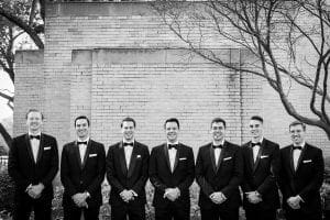 Groom and his groomsmen smiling at the camera with their hands crossed in front of them