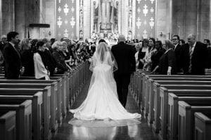 Bride and her father walking down the aisle to the altar as guests look on smilingly