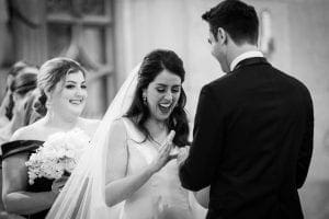Bride smiles in delight as groom slips the wedding ring on her finger