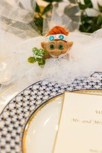 Closeup of a troll doll in lace tulle to depict a wedding dress set by a blue and white dinner plate