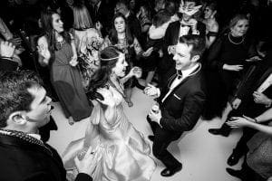 Bride and groom laughing and dancing on the floor with their guests wearing mardi gras beads and neon necklaces