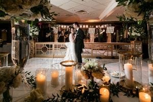 Bride and groom leaning into each other lovingly as they have their private last dance on a clear white dance floor as the band plays in the background behind them