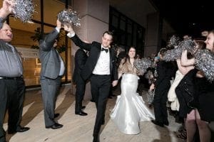  Bride and groom waving laughing and waving goodbye as guests wave silver pom poms for their exit