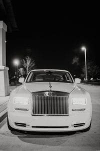 White Rolls Royce waiting in the driveway with the lights on
