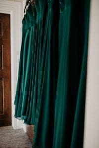 Emerald green gowns of the bridesmaids dresses hanging on a wall