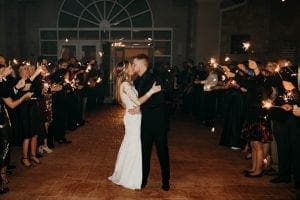  Bride and groom pausing to kiss as they exit the wedding venue as their guests hold sparklers on either side of them
