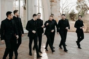  Groom and his groomsmen laughing and walking as the groom gives another groomsman a fist bump