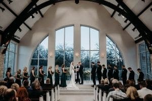 Bride groom and their bridal party standing at the altar as the officiant speaks and guests look on