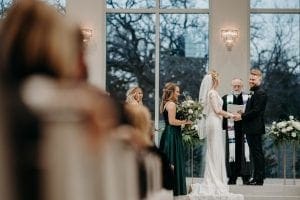 Bride and groom holding hands at the altar as the officiant reads from a passage