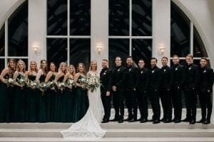 Bride groom their bridesmaids and groomsmen smiling at the camera while posing in the chapel