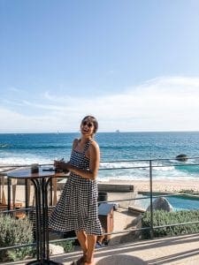 Laughing woman in a checkered sundress with the beach behind her