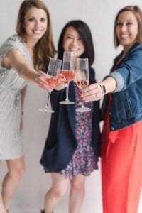 Three smiling women toasting the camera with pink champagne flutes