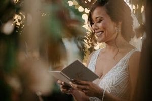 Bride smiling as she reads her vows at her wedding ceremony in the gardens of Marie Gabrielle