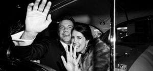 Bride and groom waving laughing and waving goodbye to guests as they are in their getaway car ready to drive off