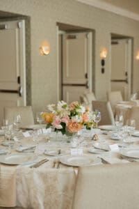 Elegant banquet table set with a pastel flower centerpiece peach pink white and arranged place settings in a cream décor hall