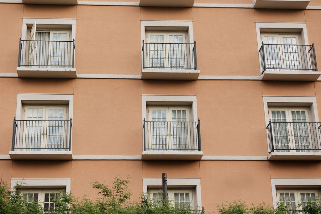 Peach colored apartment building facade with white framed doors and black metal balconies in a grid pattern