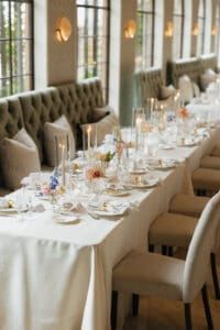 Elegant banquet table set with white tablecloth candles and floral centerpieces along a tufted sofa seating area
