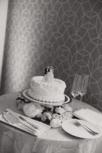 Wedding cake centerpiece with a bride and groom topper on a silver stand surrounded by flowers and formal place settings at a reception table