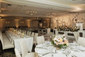 Banquet hall prepared for a formal reception long tables with white linens pastel floral centerpieces and a stage with instruments