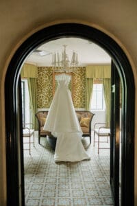 White wedding dress hanging in a luxuriously decorated room framed by an arched doorway