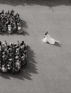 Aerial view of a wedding ceremony bride in a long gown walks toward the seated guests on a paved area