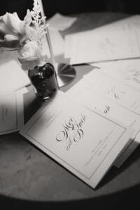 Monochrome wedding invitations fanned on a table with a small white flower vase